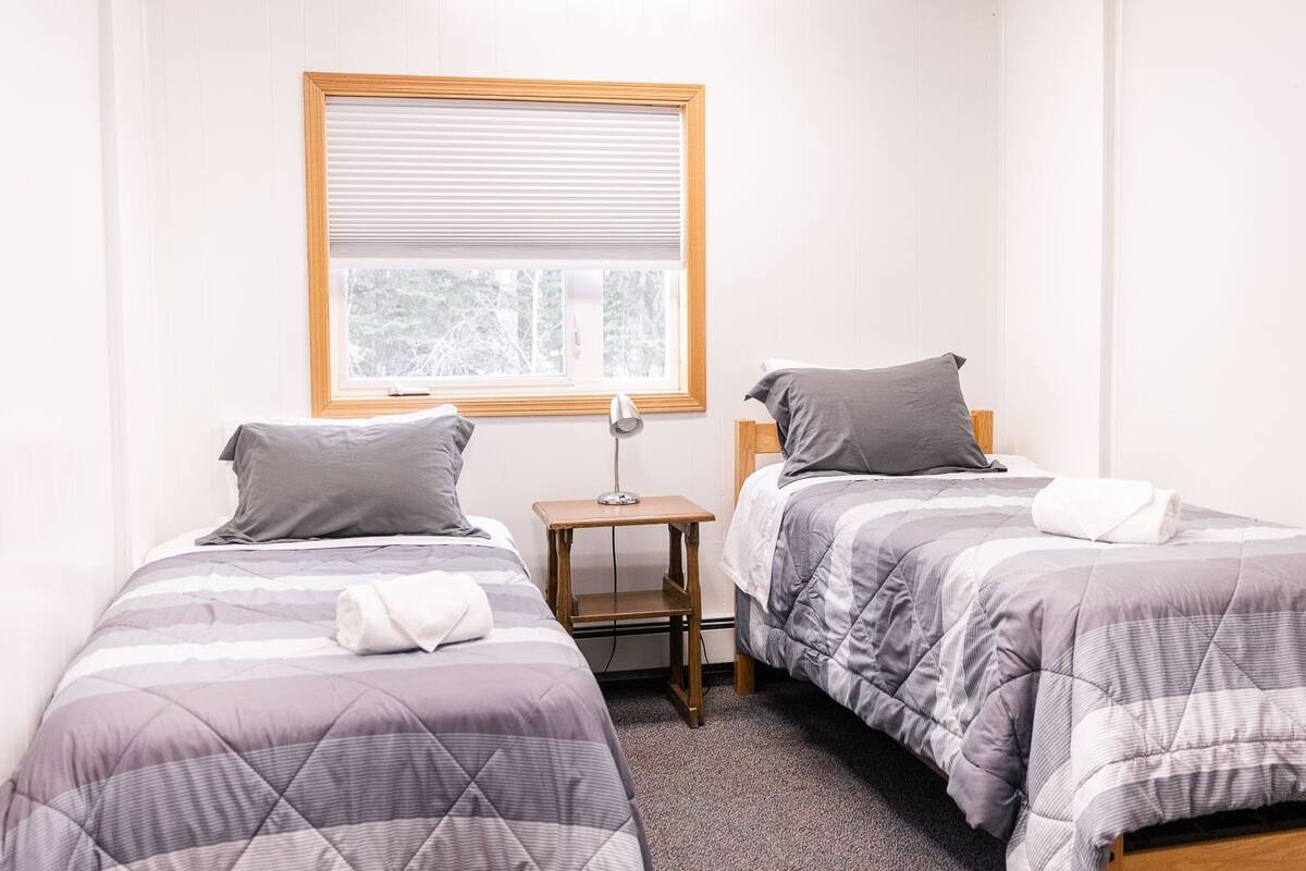 Habitación doble con dos camas, una mesita de noche y una ventana con persianas.