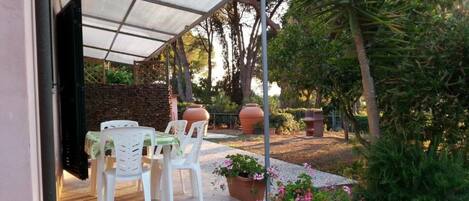 A covered patio with outdoor furniture, potted plants, and a stone pathway.