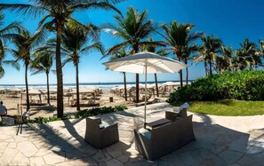 A beachside patio with outdoor seating, palm trees, and a view of the ocean.