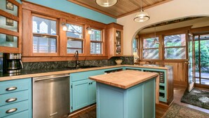 A kitchen with wooden cabinets, a built-in dishwasher, a large island with a wooden countertop, and a view of the outdoors through large windows. - A Cowslip's Belle Inn (Ashland)