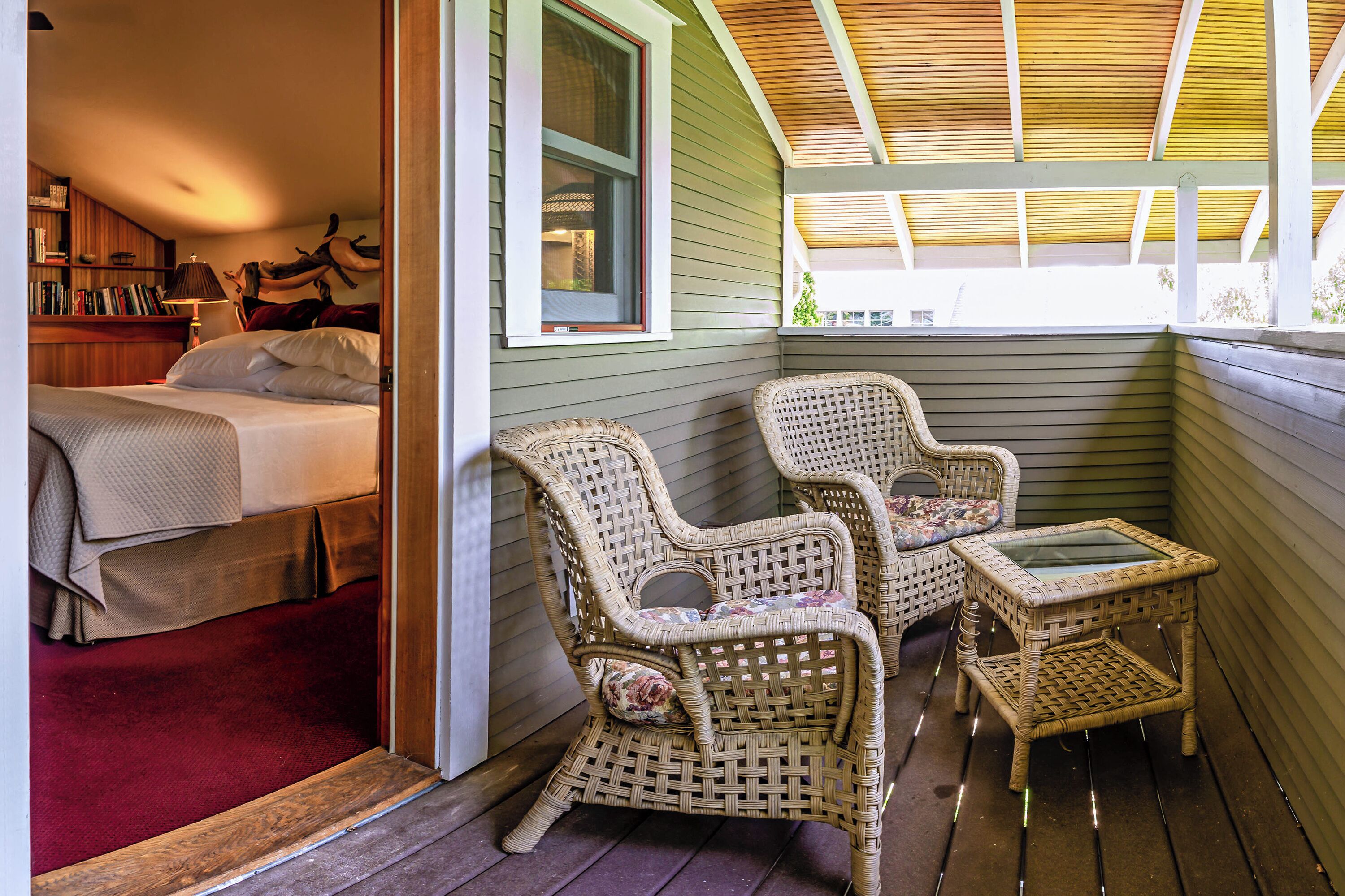 Ein Zimmer mit einem Bett, einem kleinen Tisch, zwei Korbstühlen und einem Fenster.