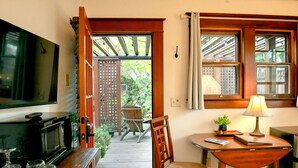 A room with a television, a wooden table with a lamp, a chair, and a small plant. There is a wooden door leading to an outdoor area with a chair and a table. - A Cowslip's Belle Inn (Ashland)