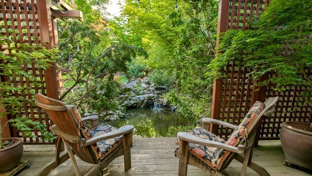 Two rocking chairs facing a pond with a waterfall, surrounded by lush greenery and wooden fences. - A Cowslip's Belle Inn (Ashland)