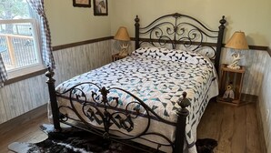 A bedroom with a bed, two bedside lamps, a ceiling fan, a window with curtains, and a wall-mounted picture. - Whispering Wind Cabin where peacefulness and relaxation surrounds you (Pfeifer)