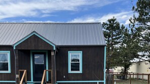 A rustic wooden building with a dark facade and teal trim, featuring a front porch and a metal roof. - Whispering Wind Cabin where peacefulness and relaxation surrounds you (Pfeifer)