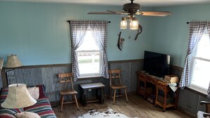 A cozy living room with a sofa, chairs, a television, and a ceiling fan. - Whispering Wind Cabin where peacefulness and relaxation surrounds you (Pfeifer)
