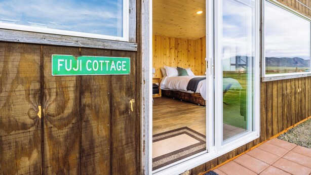 Rakennuksen ulkoseinät ovat puuta, ja siinä on kyltti, jossa lukee ”FUJI COTTAGE”. Näkyvissä on myös makuuhuoneen sisustus, jossa on sänky ja ikkuna.