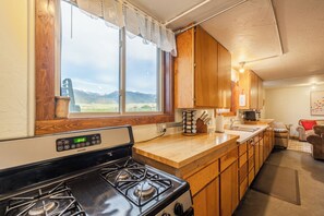 Cocina compacta con armarios de madera, estufa y ventana con vistas a las montañas.