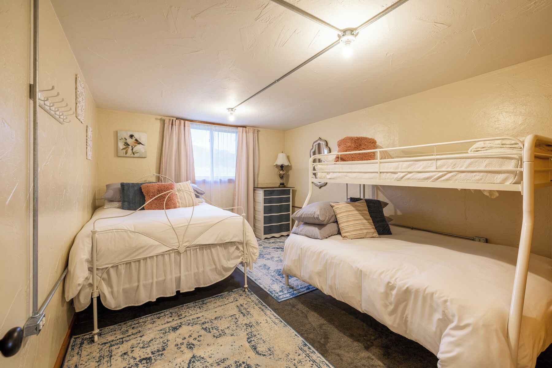 A bedroom with two beds, a nightstand, a dresser, and a window with curtains.