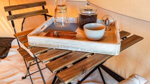 A wooden table with a tray holding a glass carafe, a metal cup, a ceramic mug, and a small container.