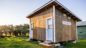A rustic wooden bath house with a white door and a sign reading "BATH HOUSE" on the side.