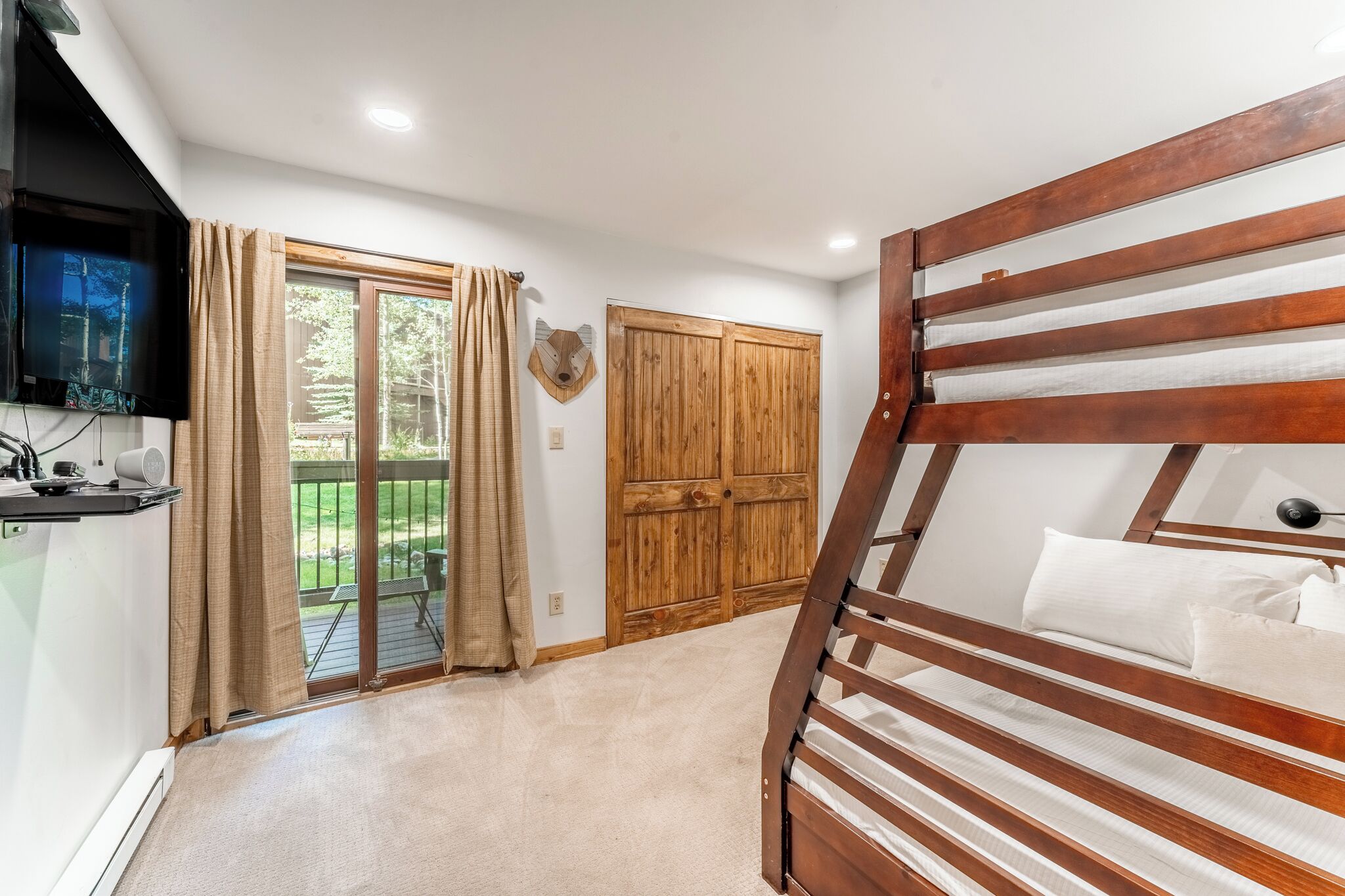 A bedroom with a bunk bed, a wooden wardrobe, a television, and a sliding glass door leading to an outdoor area.