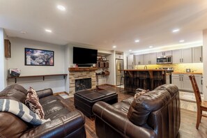 Una sala de estar moderna con sofás de cuero, una chimenea y una cocina con taburetes de bar.