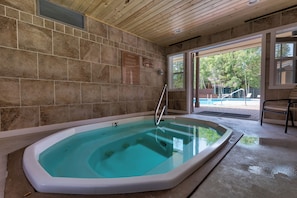 Área de spa com hidromassagem, paredes de pedra e vista para um quintal com piscina.