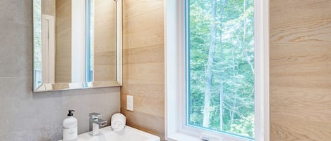 A bathroom with a white sink, a mirror, and a window with a view of trees.