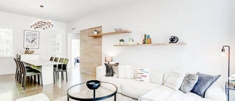 Una sala de estar moderna con un sofá blanco, una mesa de centro de vidrio y un comedor con una mesa y sillas blancas.