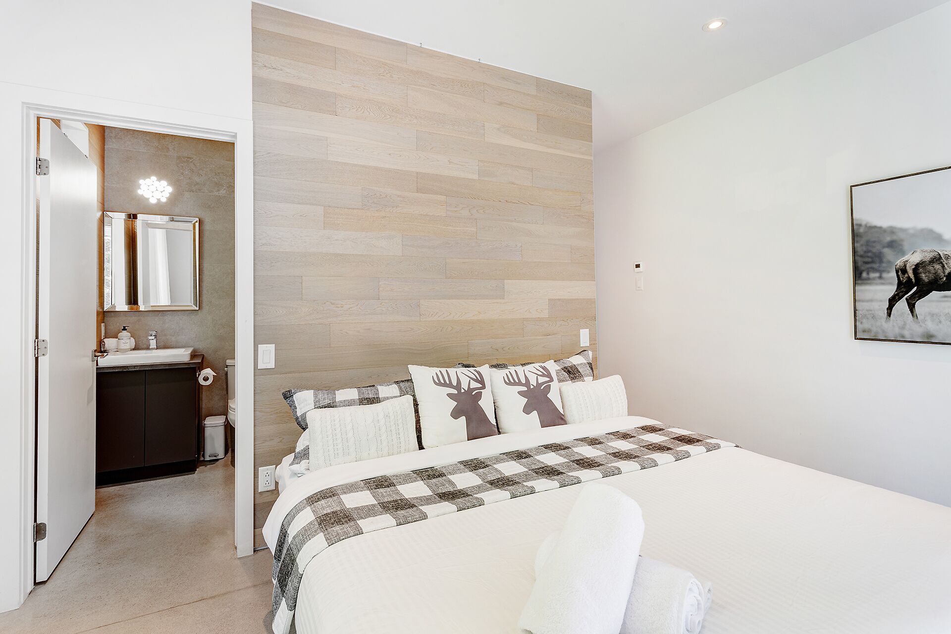A bedroom with a wooden headboard, a bed with a checkered blanket, a white bedside table, and a bathroom visible through an open door.