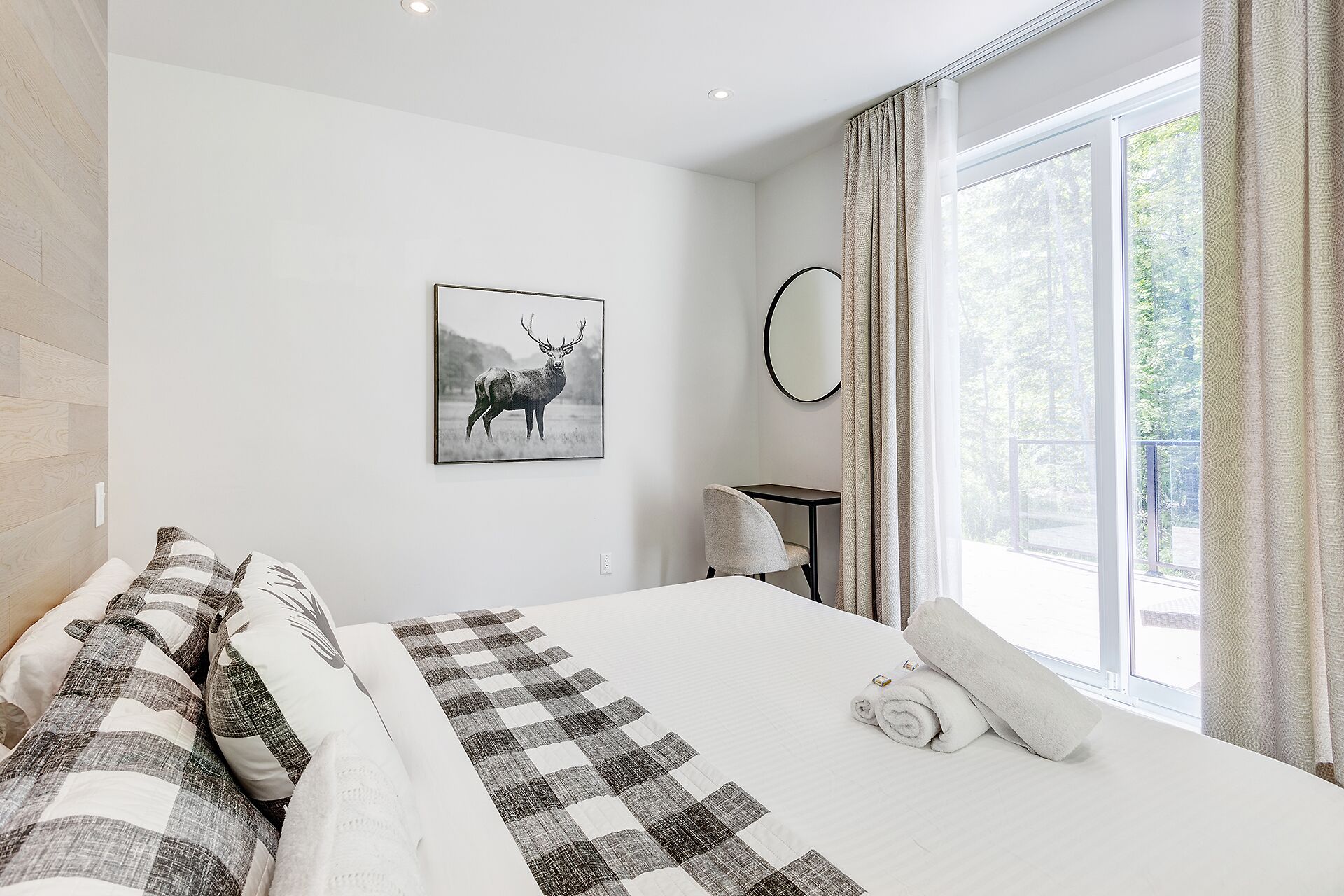 Un dormitorio con cama, escritorio, silla, espejo y ventana con cortinas.