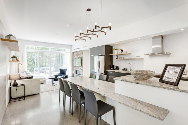 A modern kitchen with a large island, built-in appliances, and a stone backsplash. - Tremblant Oasis: Luxury, Nature, Hot Tub, Views! (La Conception)