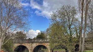 Eine Reihe von Booten am Flussufer, im Hintergrund eine Steinbrücke.