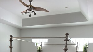 Una cama con dosel y tablero de madera, un ventilador de techo y una ventana con plantas.