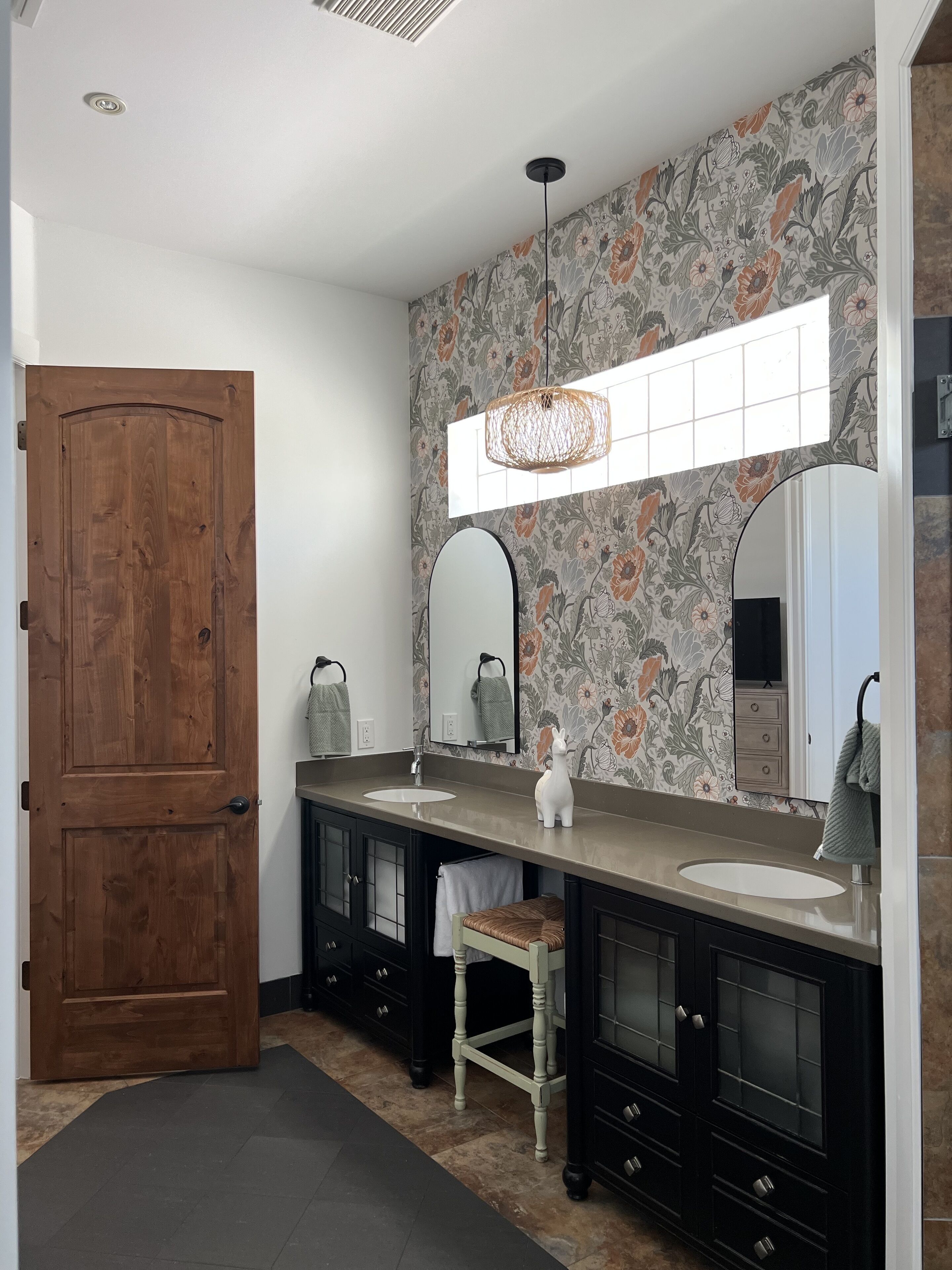 Un baño con puerta de madera, un espejo grande, un lavamanos y un adorno en la pared.