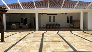 Un patio cubierto con suelo de baldosas, una mesa de comedor con sillas y un ventilador de techo.
