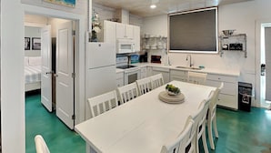 A compact kitchen with white cabinets, a dining table with chairs, and a small island with a bowl of fruit. - 7 Heaven by Silver Sands Vacation Rentals (Port Aransas)