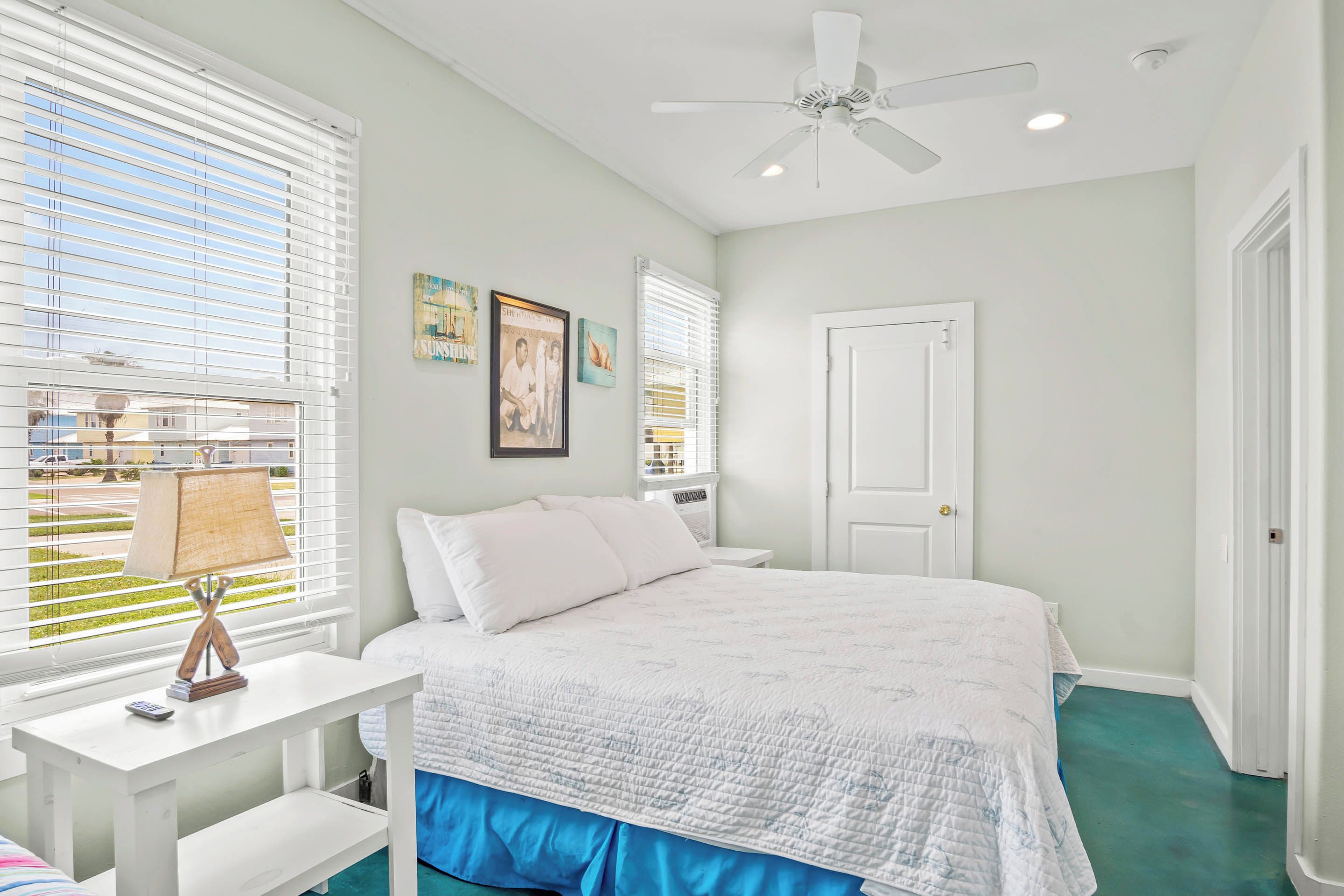 A bedroom with a bed, white walls, a ceiling fan, and a window with blinds.