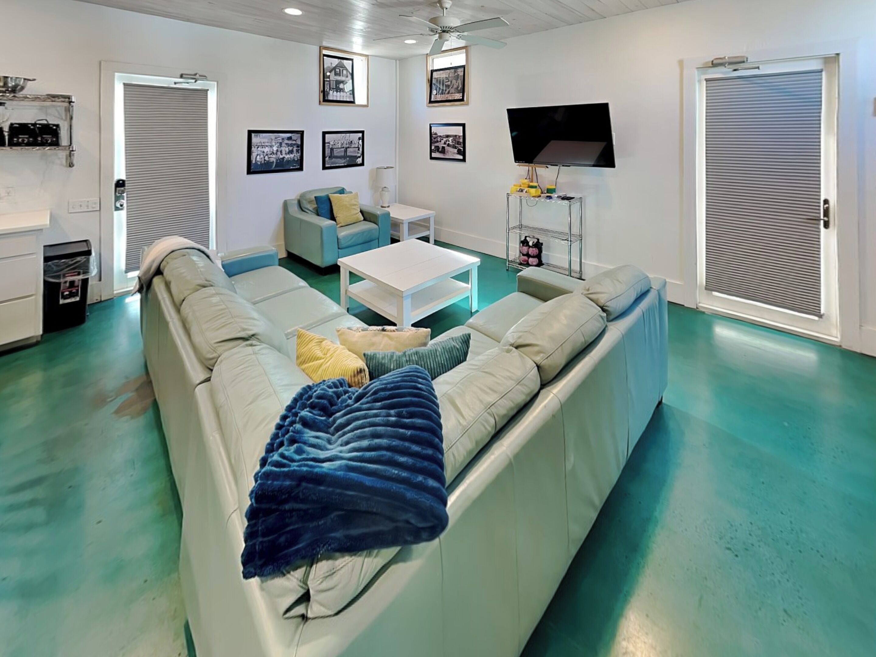 Una sala de estar moderna con un sofá modular, una mesa de centro y un televisor de pantalla plana. Se observan cuadros enmarcados en la pared y un ventilador de techo.