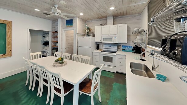 A modern kitchen with white cabinetry, a dining area with a white table and chairs, and a green floor. - 7 Heaven by Silver Sands Vacation Rentals (Port Aransas)