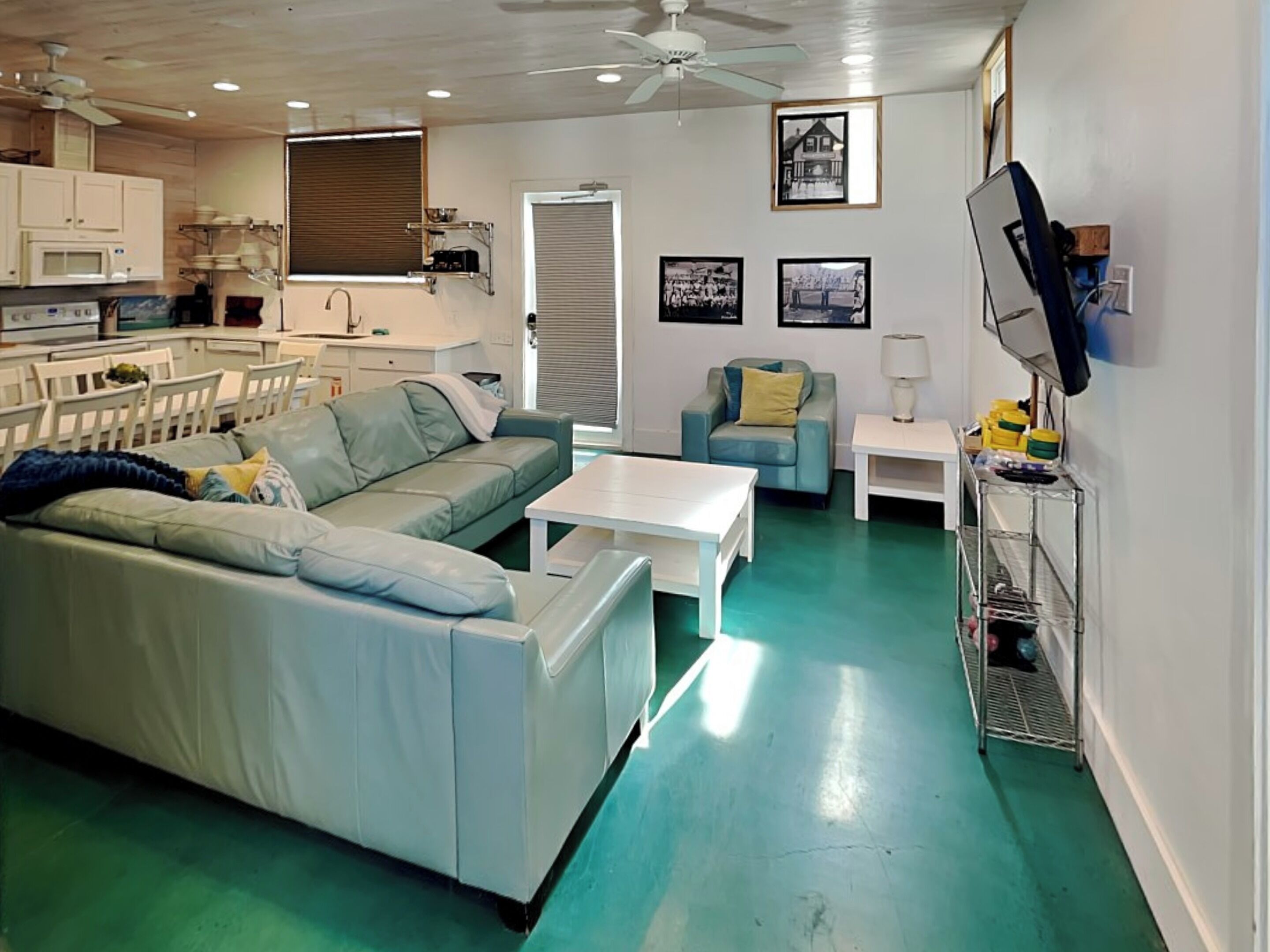 A living room with a green floor, a white sofa, a blue armchair, a white coffee table, and a TV on a stand.