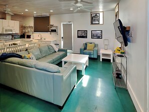 A living room with a green floor, a white sofa, a blue armchair, a white coffee table, and a TV on a stand. - 7 Heaven by Silver Sands Vacation Rentals (Port Aransas)