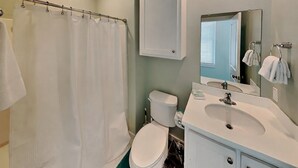 A bathroom with a shower curtain, toilet, sink, and mirror. - 7 Heaven by Silver Sands Vacation Rentals (Port Aransas)