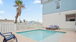 A rectangular swimming pool with a white fence, two lounge chairs, and a palm tree. - 7 Heaven by Silver Sands Vacation Rentals (Port Aransas)