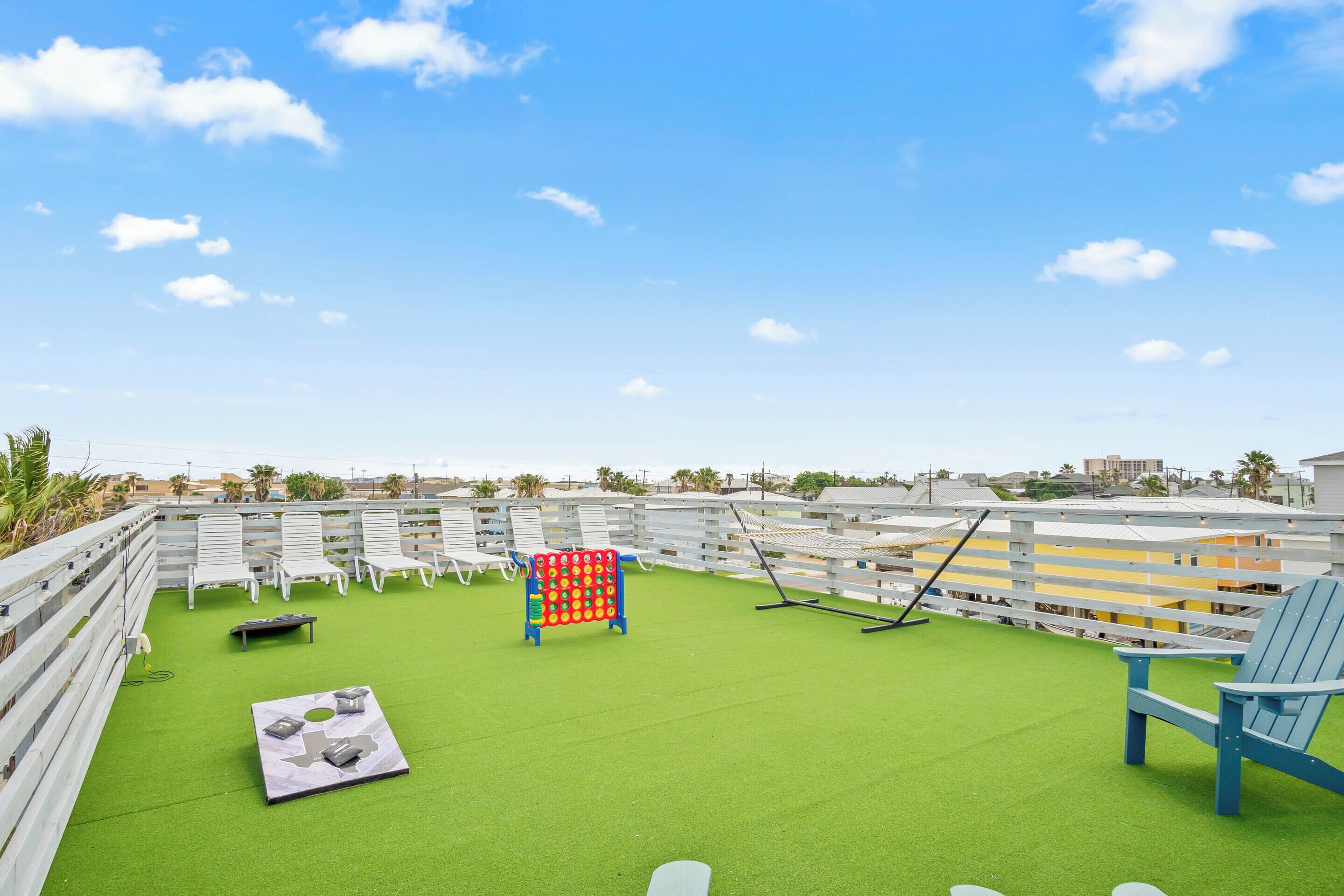 A rooftop deck with green artificial turf, white lounge chairs, and a colorful play structure.