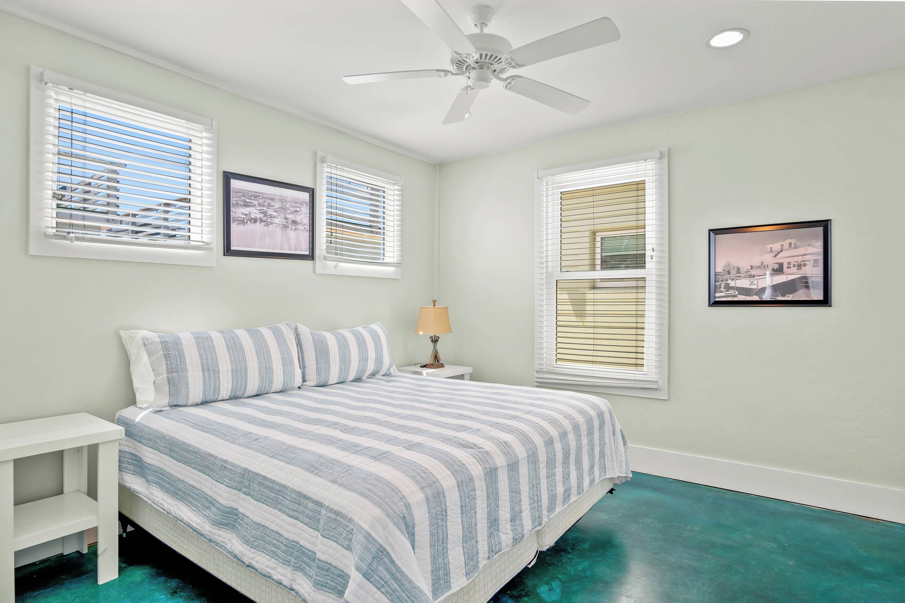 A bedroom with a bed, a nightstand, a ceiling fan, and two windows with blinds.