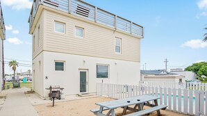 A two-story building with a white exterior, a balcony, a fenced pool area, and a picnic table. - Above & Beyond by Silver Sands Vacation Rentals (Port Aransas)