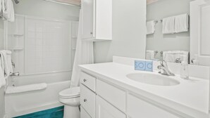 A modern bathroom with a white sink, mirror, and toilet. There are white towels hanging on the wall and a shower curtain. - Above & Beyond by Silver Sands Vacation Rentals (Port Aransas)