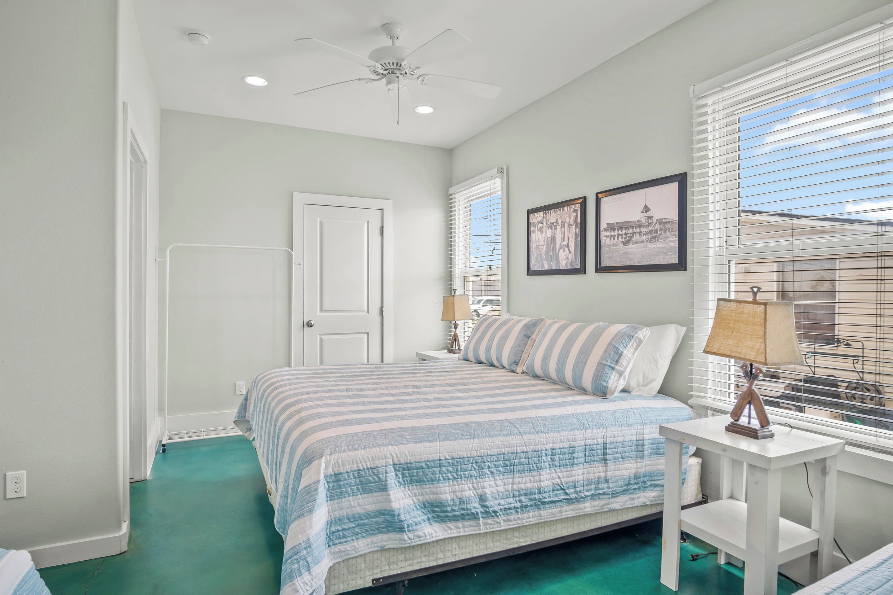 A bedroom with a bed, a ceiling fan, a window with blinds, and a nightstand with a lamp.