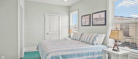 A bedroom with a bed, a ceiling fan, a window with blinds, and a nightstand with a lamp.