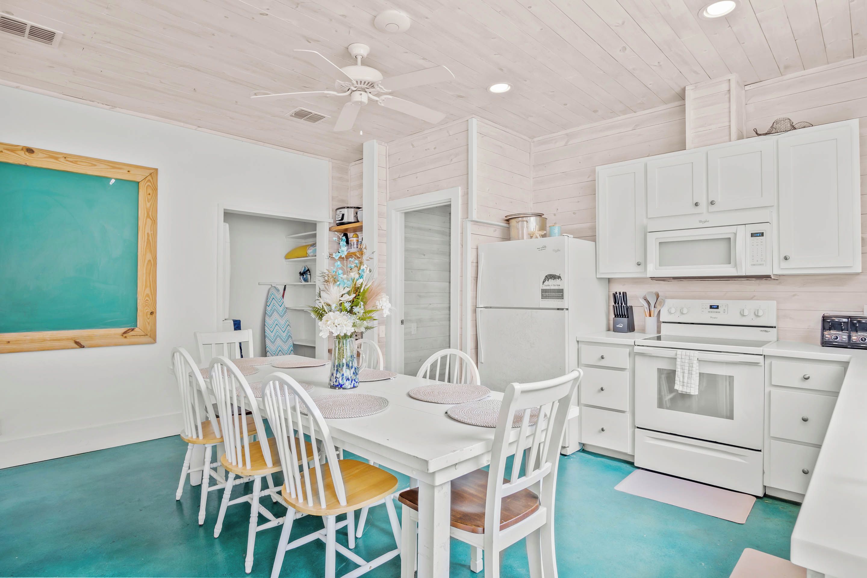 A kitchen with white cabinets, a white refrigerator, a microwave, and a stove. There is a dining table with white chairs and a vase with flowers.