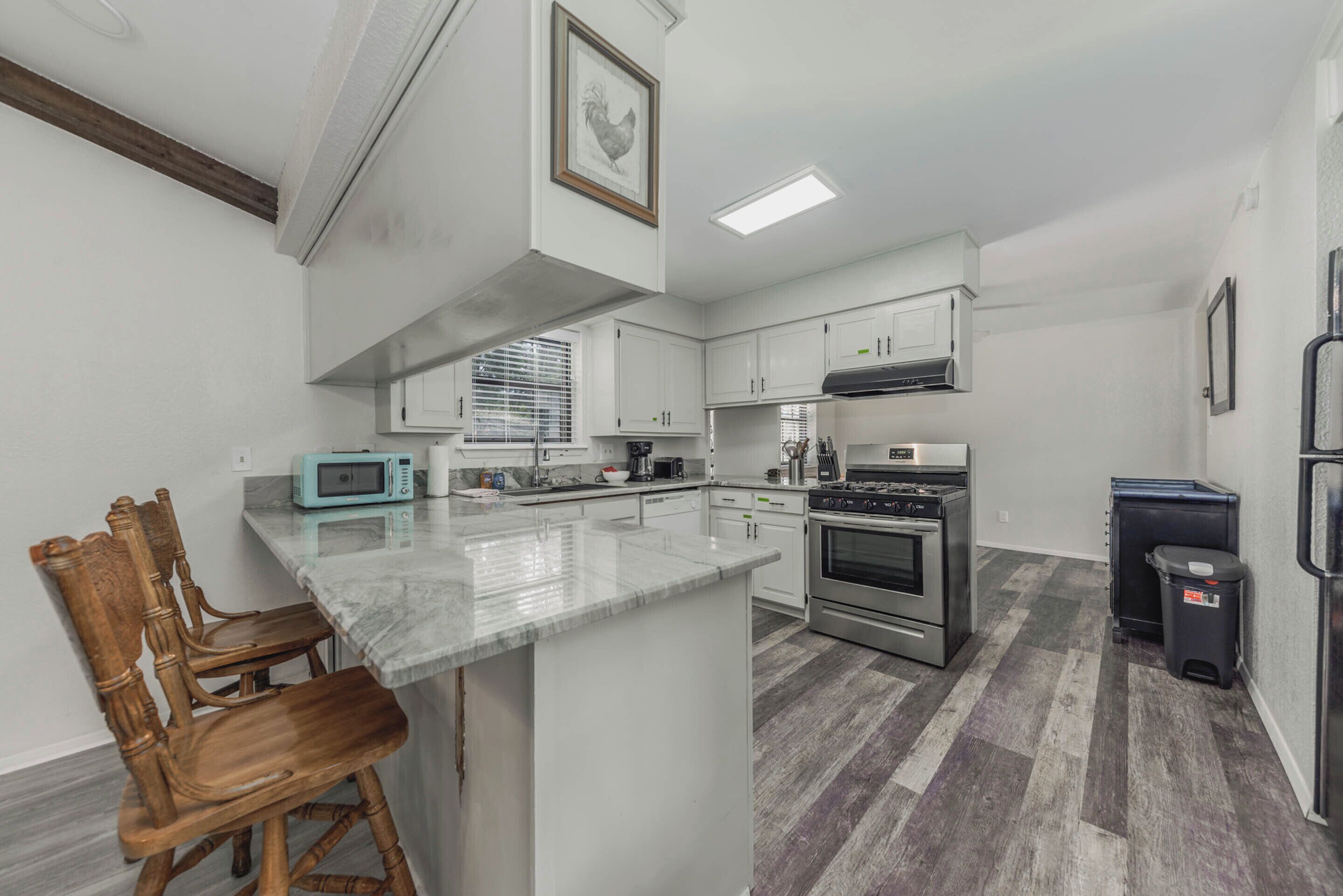 A kitchen with white cabinets, a built-in microwave, a stove, and a trash bin.