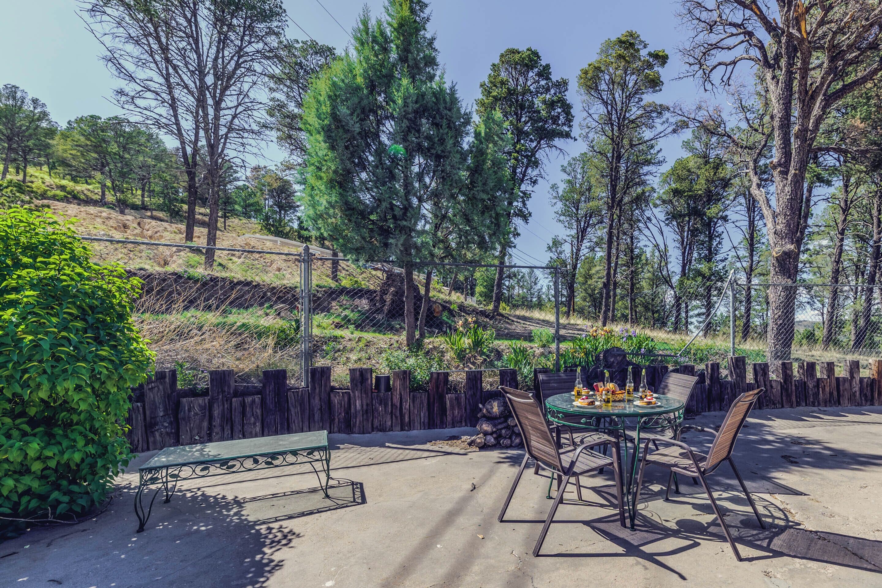 Une terrasse extérieure avec une table et des chaises, entourée d’une clôture en bois et d’arbres.