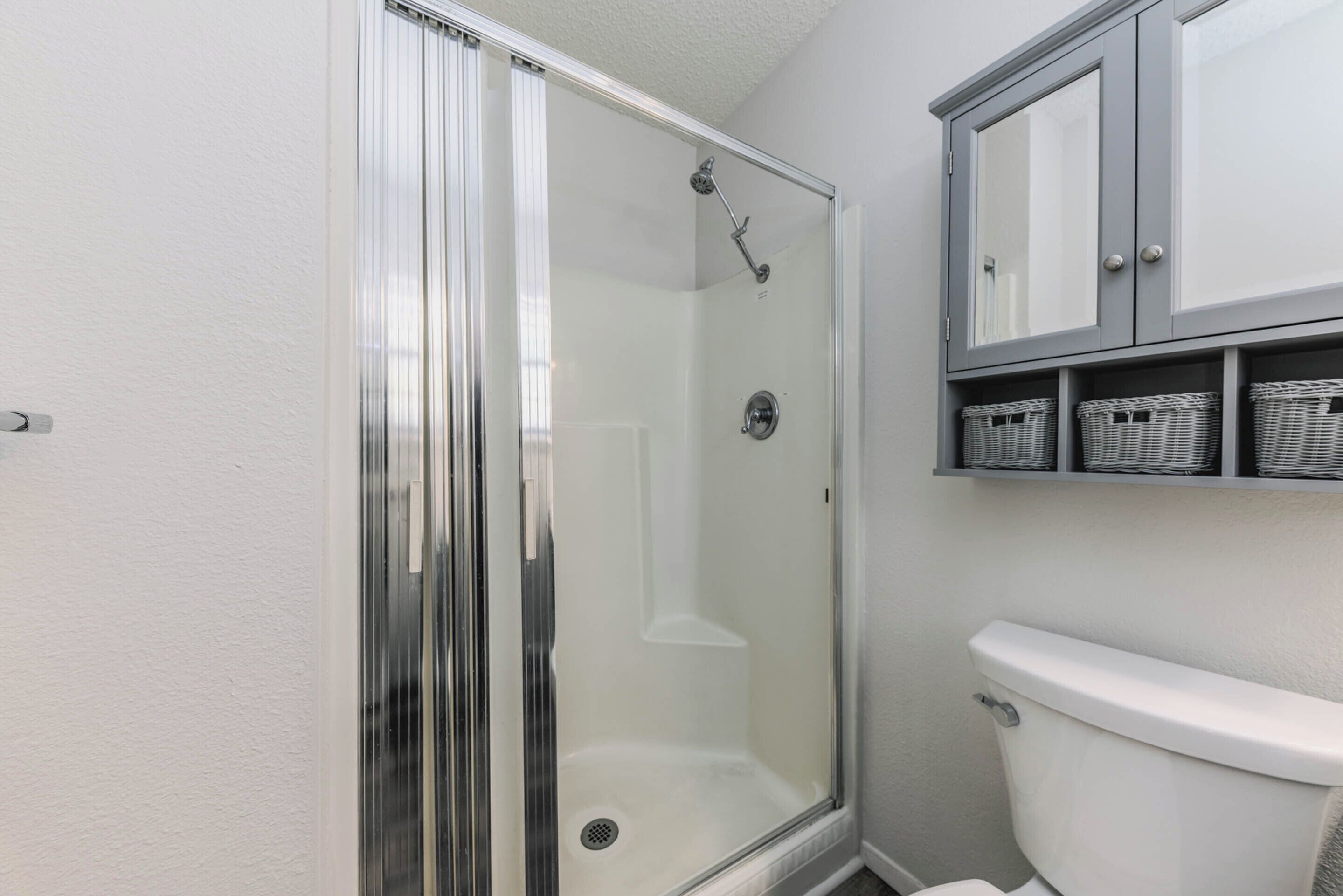 Ein Badezimmer mit einer Glaskabine zur Dusche, einer weißen Toilette und einem Schrank mit Korbkörben.