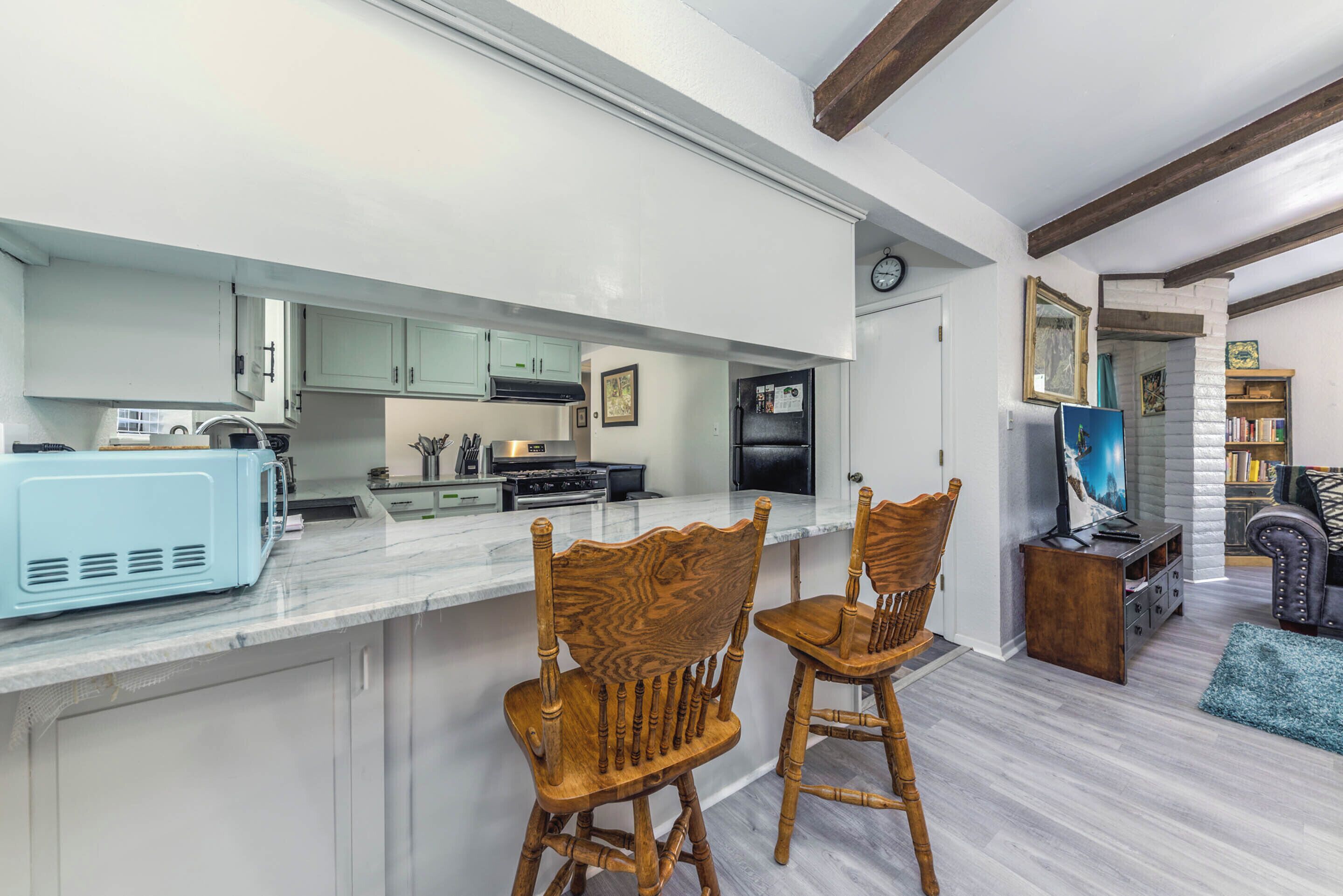 A modern kitchen with white cabinets, a blue microwave, and wooden chairs.