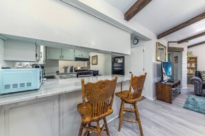 A modern kitchen with white cabinets, a blue microwave, and wooden chairs. - Castle House by Ruidoso Vacation Rentals (Ruidoso)
