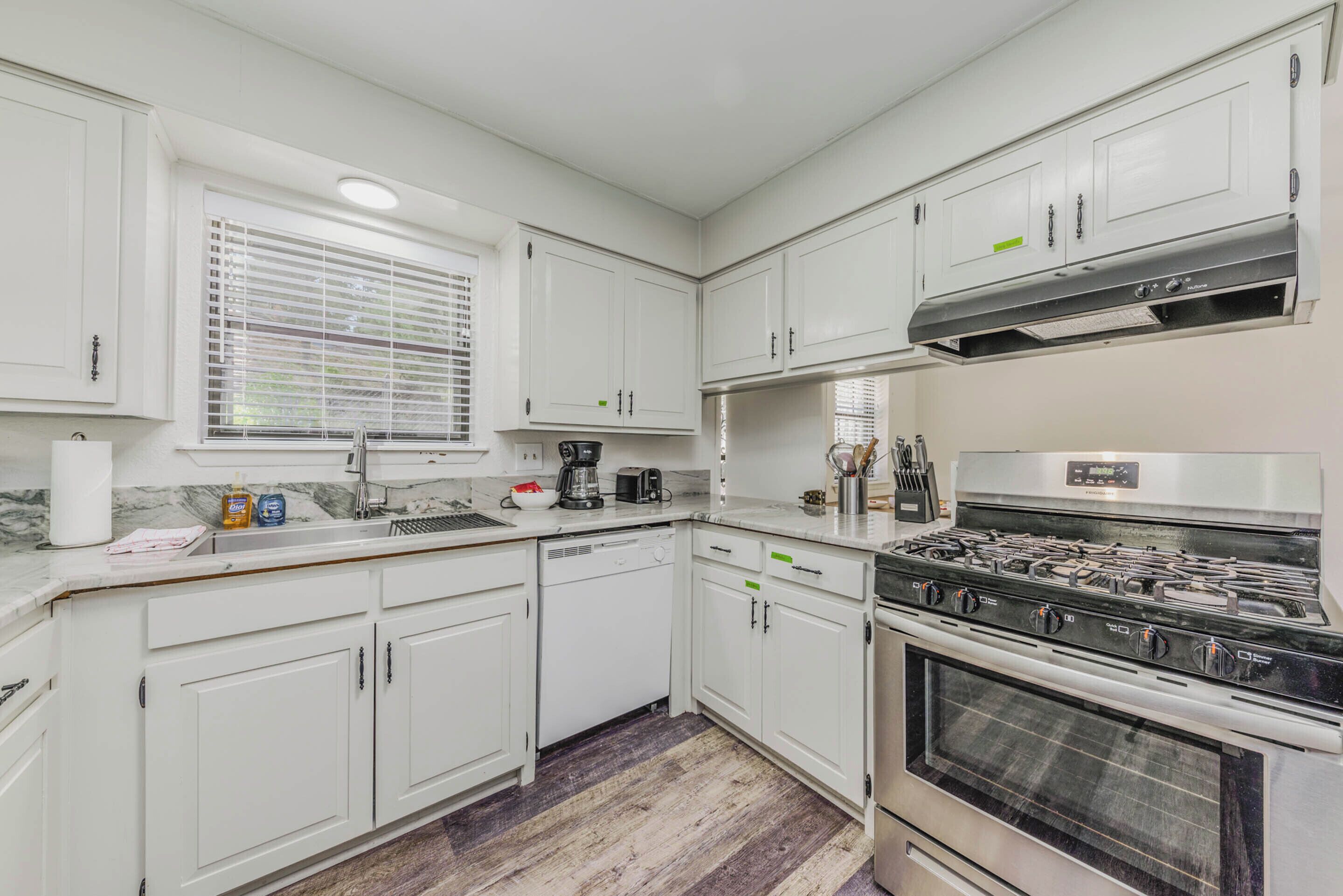 A modern kitchen with white cabinets, a built-in oven, and a window with blinds.