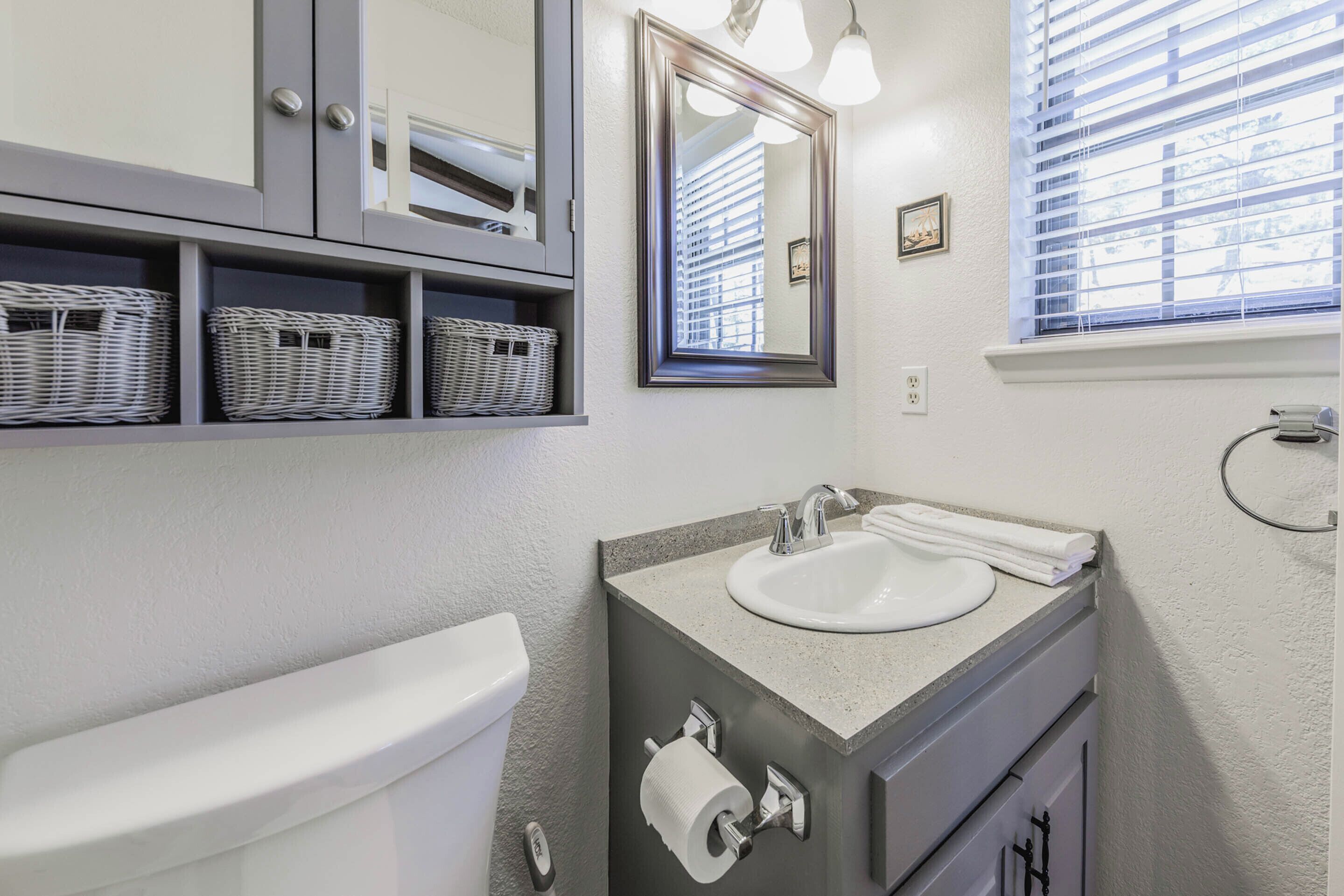 Een badkamer met toilet, wastafel, spiegel en rieten manden op planken.