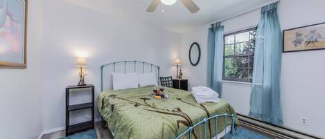 A bedroom with a bed, two bedside tables, a ceiling fan, a window with curtains, and a framed picture on the wall.